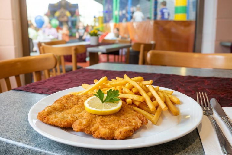 Schnitzel Wiener Art mit Pommes und Zitrone auf einem Teller im Restaurant des Freizeitparks Landsberg, im Hintergrund das Kinderparadies