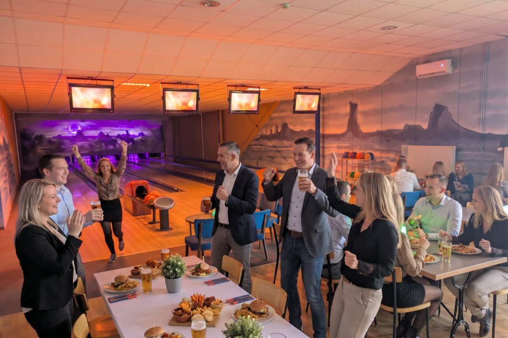 Teamevent im Freizeitpark Landsberg: Kollegen jubeln an der Bowlingbahn über einen Strike, daneben eine Tafel mit Burgern und Getränken