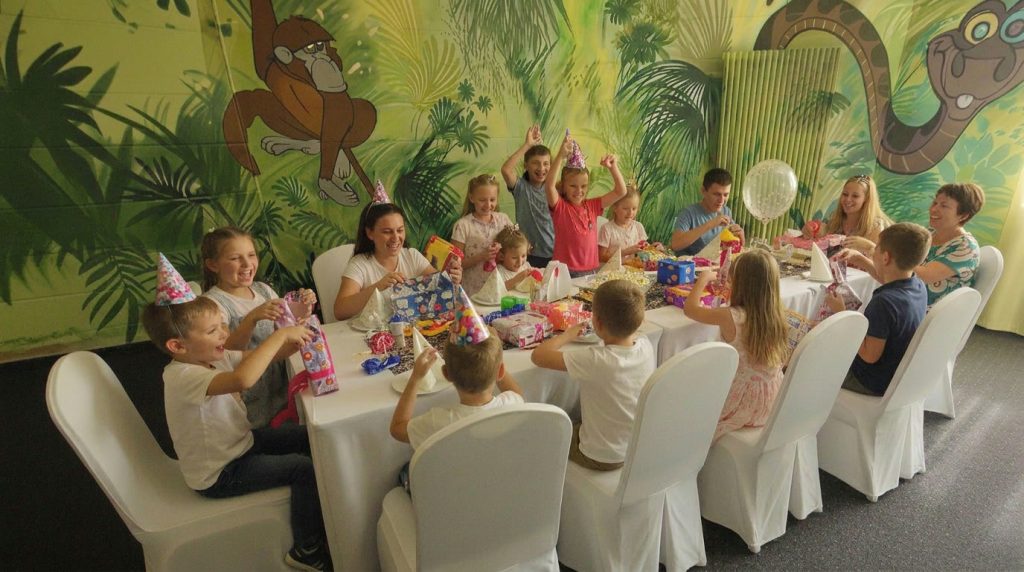 Kindergeburtstag im Freizeitpark Landsberg bei Leipzig und Halle: Kinder feiern am festlich gedeckten Tisch vor der Dschungel-Wandmalerei